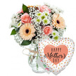 The photograph presents a serene yet festive Mother's Day arrangement, composed with the eye of a seasoned local florist. Against a pure white background, a clear glass vase filled with water supports a generous bouquet of mixed flowers. The vase is simple and transparent, its only decoration a slim piece of rustic twine tied casually around the neck, suggesting an easy, natural style that suits Grove Park's relaxed, leafy character. Above the glass, the bouquet forms a soft dome of pastels and whites. Peach-pink roses are scattered throughout, some fully open to reveal spiralling petals, others in mid-bloom, which adds depth and variation. Interwoven with the roses are several peach and apricot gerbera daisies. Their broad petals radiate around dark, velvety centres, giving the arrangement playful focus points. Light, feathery sprays of white baby's breath fill the spaces between, creating a gentle haze, while small white chrysanthemums with delicate pale green centres bring clarity and crispness, much like the fresh air along the nearby Thames Path. Glossy green foliage emerges from beneath and between the blooms, adding structure and a natural frame. Slightly behind the flowers, a small white card with hints of colourful, mostly illegible writing suggests a personal Mother's Day note, private and heartfelt. To the right, resting in front of the vase, a large heart-shaped foil balloon commands attention. Its white surface is decorated with scattered metallic gold and silver dots, catching light like tiny celebrations. At the centre of the balloon sits a peach-toned heart enclosing the words HAPPY Mother's DAY in strong black letters, the word Mother's flowing in a graceful script. The arrangement feels poised and ready to be given, as if it might be carried from Grove Park Florist straight to a mother's doorstep, bringing joy into her living room.